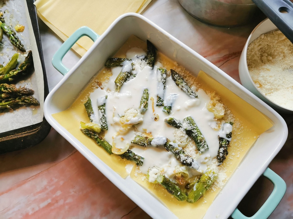Grated Parmigiano and béchamel on top of asparagus, leeks and pasta sheets in oven dish.