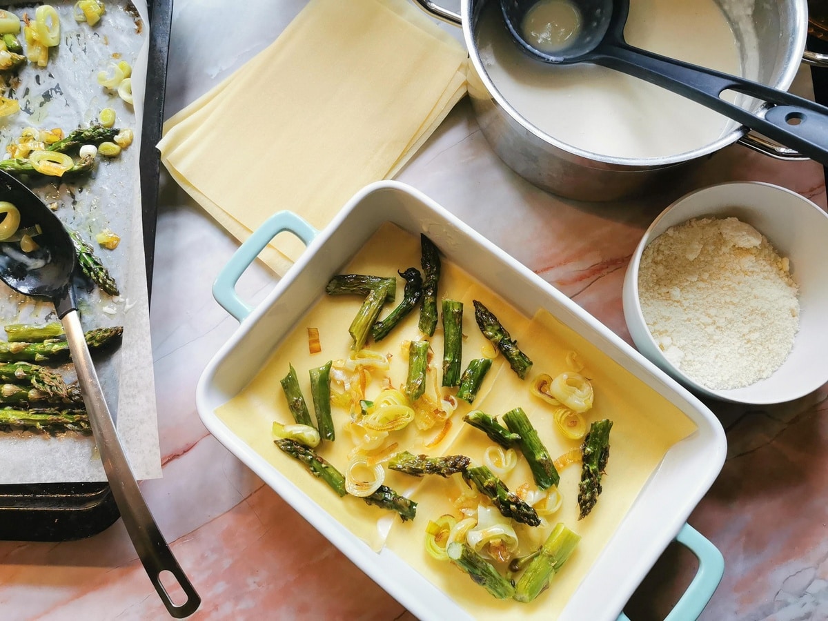 Pieces of asparagus and leeks on top of lasagne sheets in oven dish.