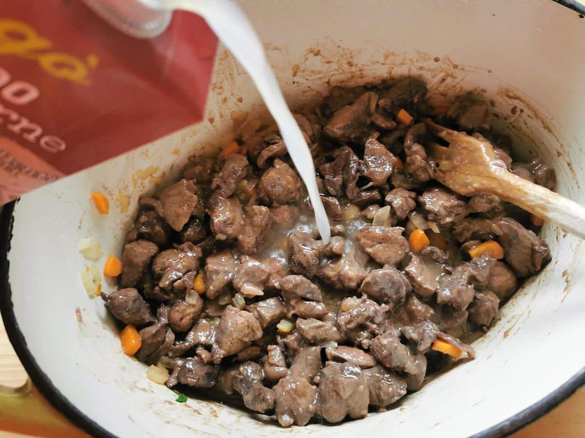 Beef broth being poured into Dutch oven over the hare and vegetables.