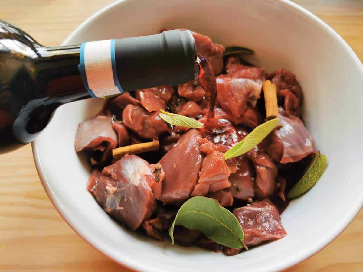 Red wine being poured into bowl with hare, spices and herbs.