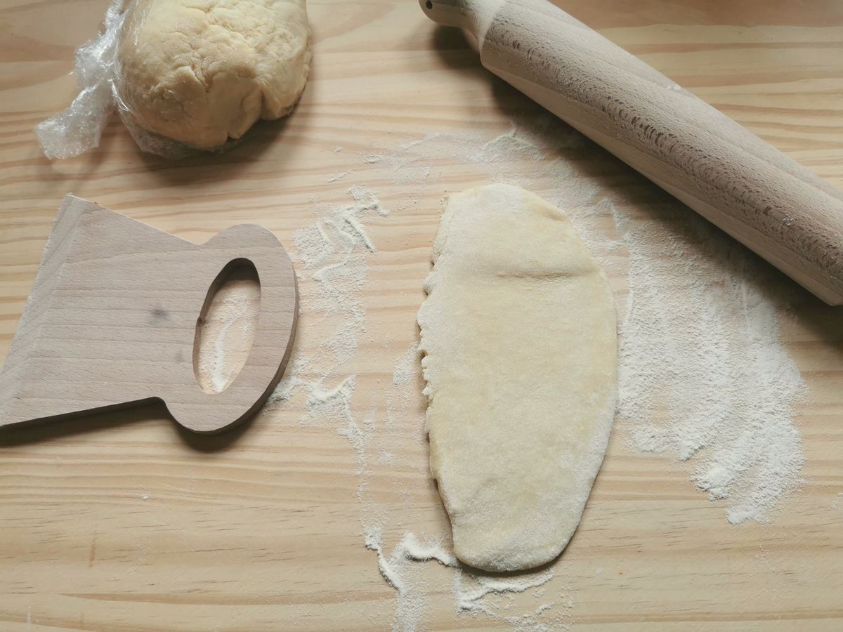A flattened piece of casoncelli dough on flour dusted wood work surface with a rolling pin and dough cutter.