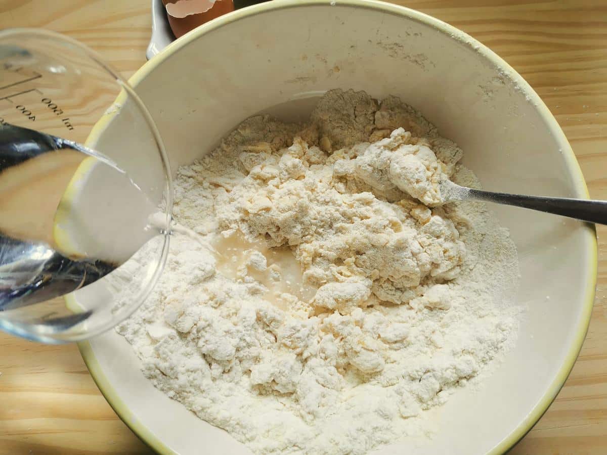 Flour and eggs mixed together in white bowl while water is added.