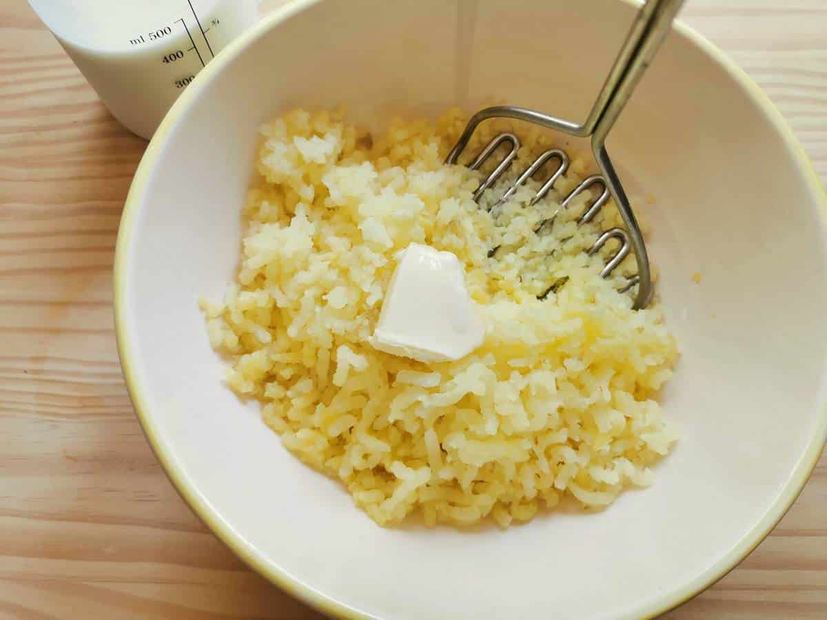 Potatoes and butter being mashed into a bowl.