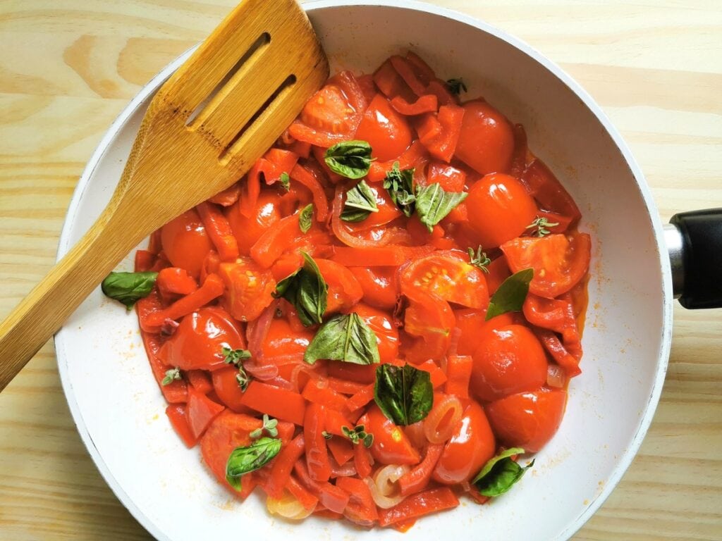 Fresh basil, tomatoes, onions and red peppers cooking in frying pan.