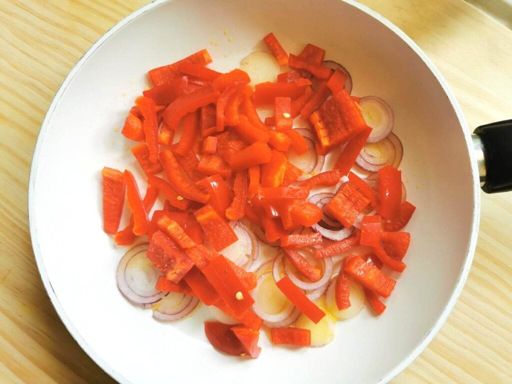Chopped red peppers and onions in frying pan.