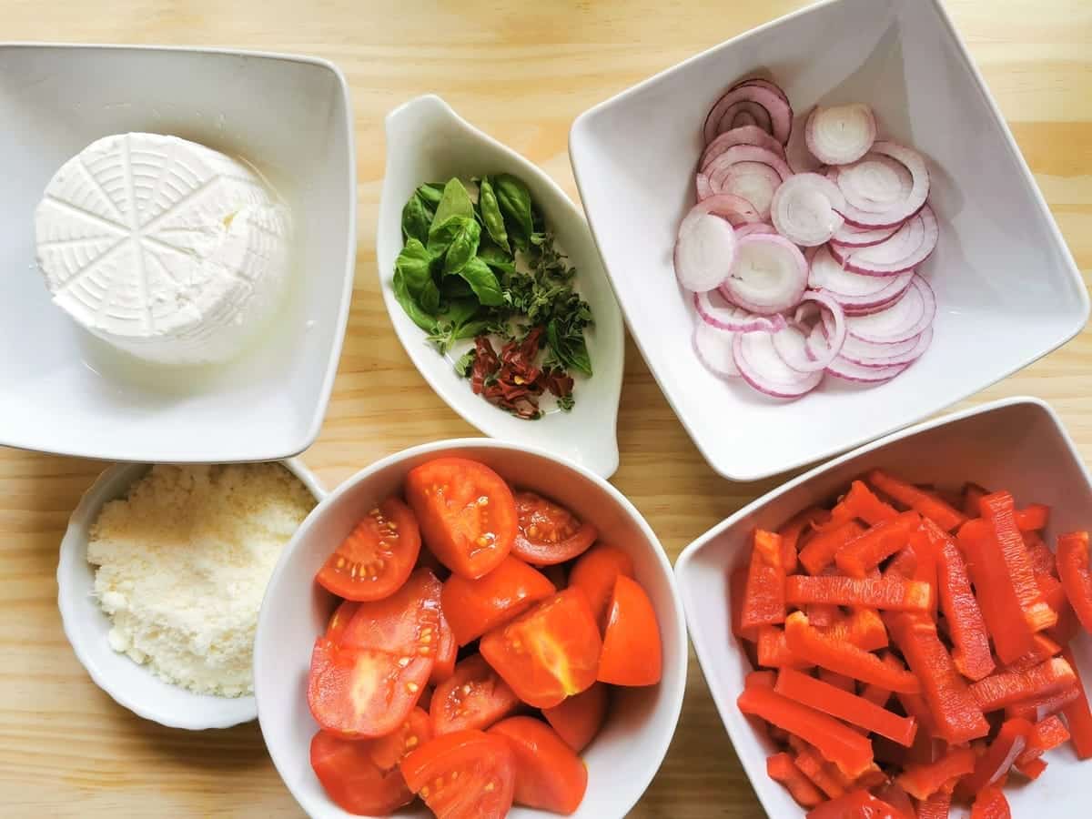 Chopped tomatoes, red peppers, onions and herbs in white bowls plus ricotta and grated pecorino in white bowls.