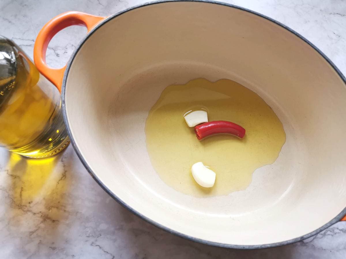 Peeled garlic cloves and half a peperoncino in a Dutch oven with olive oil.