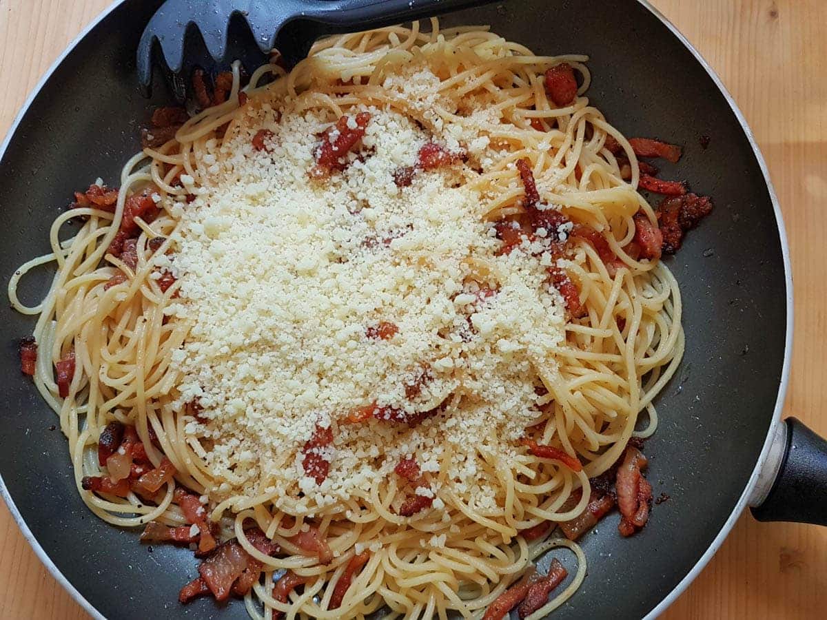 Adding Pecorino to the spaghetti and guanciale.