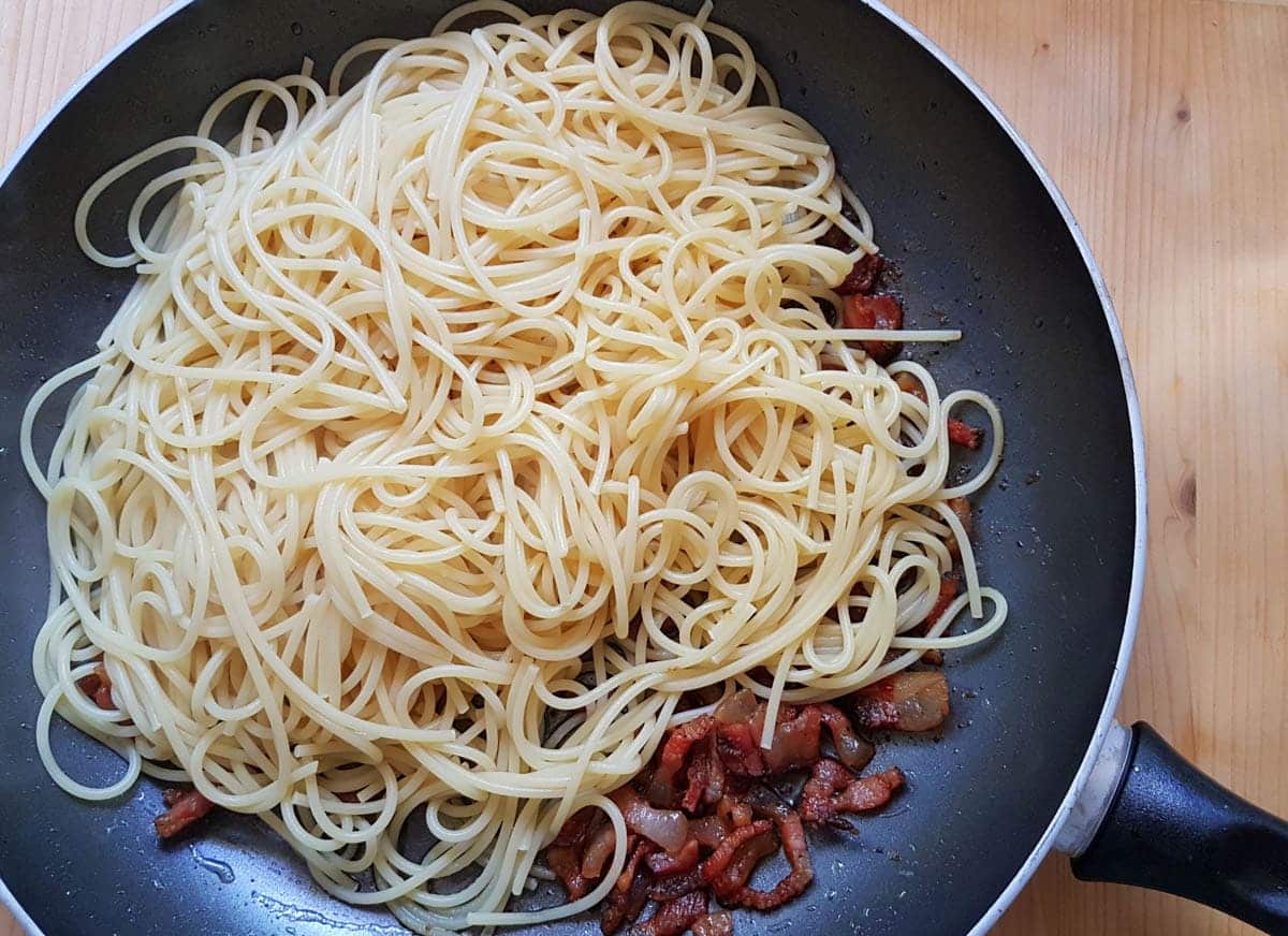 Cooked spaghetti and guanciale in frying pan.