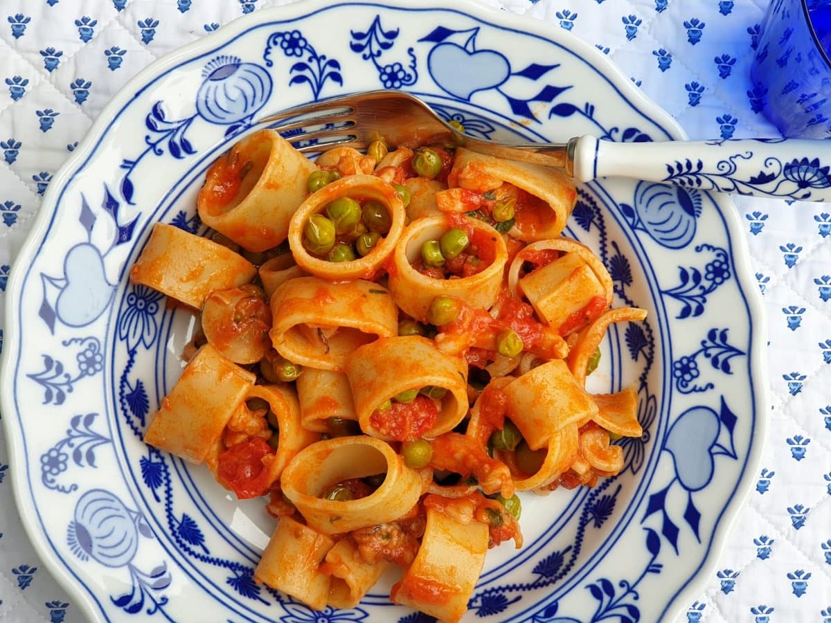 Pasta with stewed cuttlefish and peas in blue and white bowl.