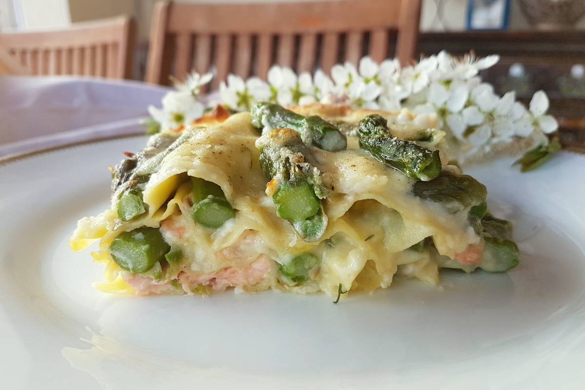 Poached salmon and asparagus lasagna on white plate.