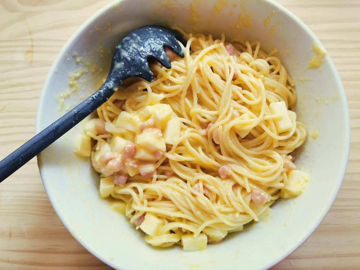 Cooked spaghetti in white bowl  mixed with eggs, cheese and pancetta.